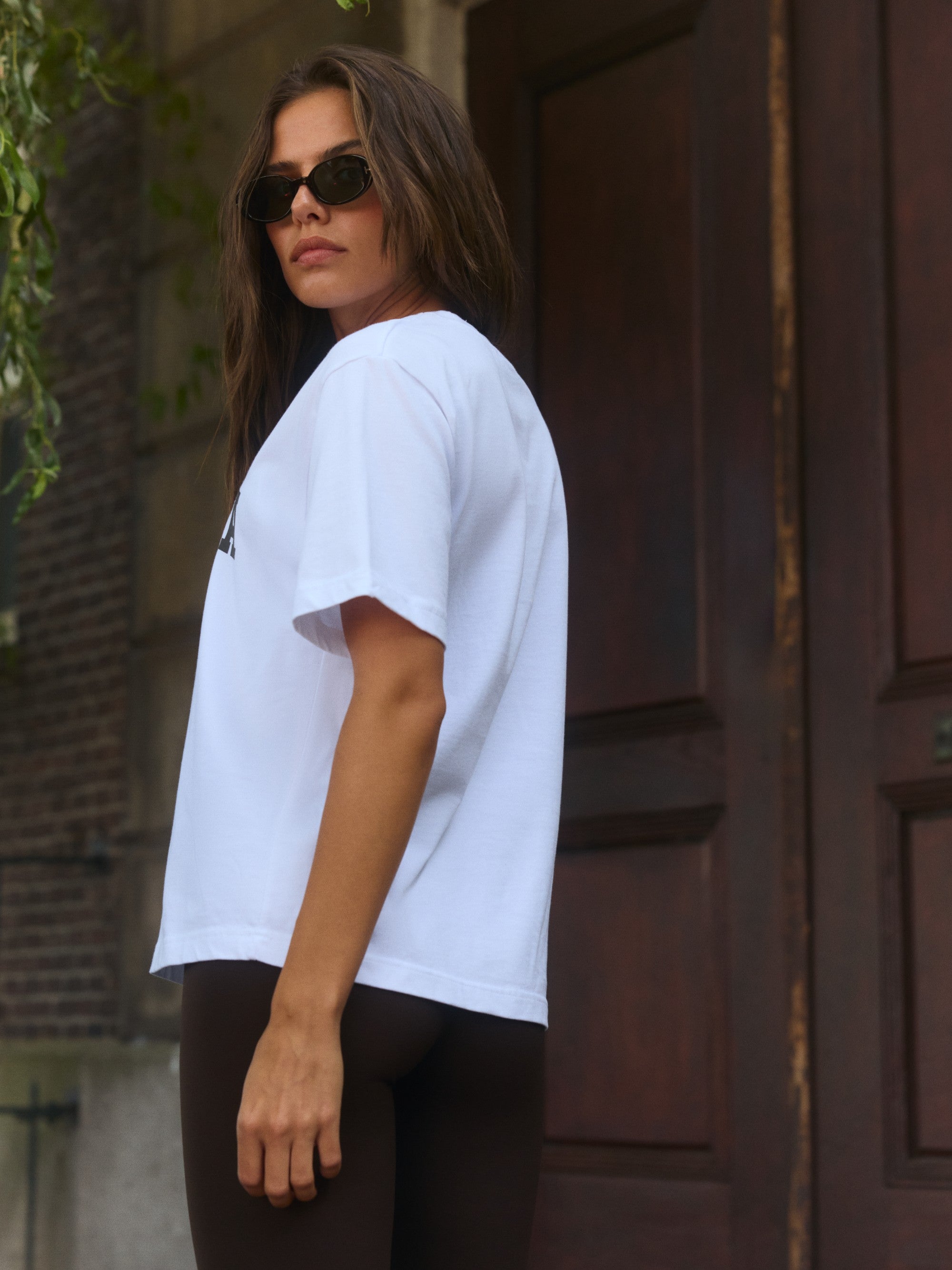 Woman wearing a white CASPARA signature t-shirt and sunglasses outdoors.